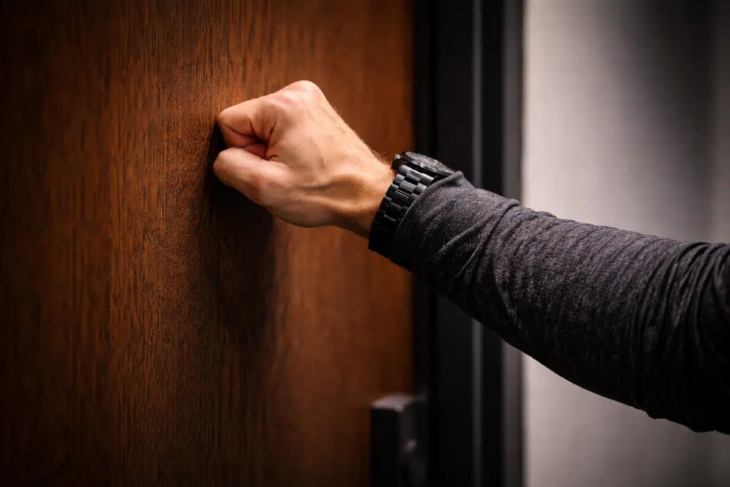 Close-up of a hand knocking firmly on a wooden door, representing grit, persistence, and sales effort